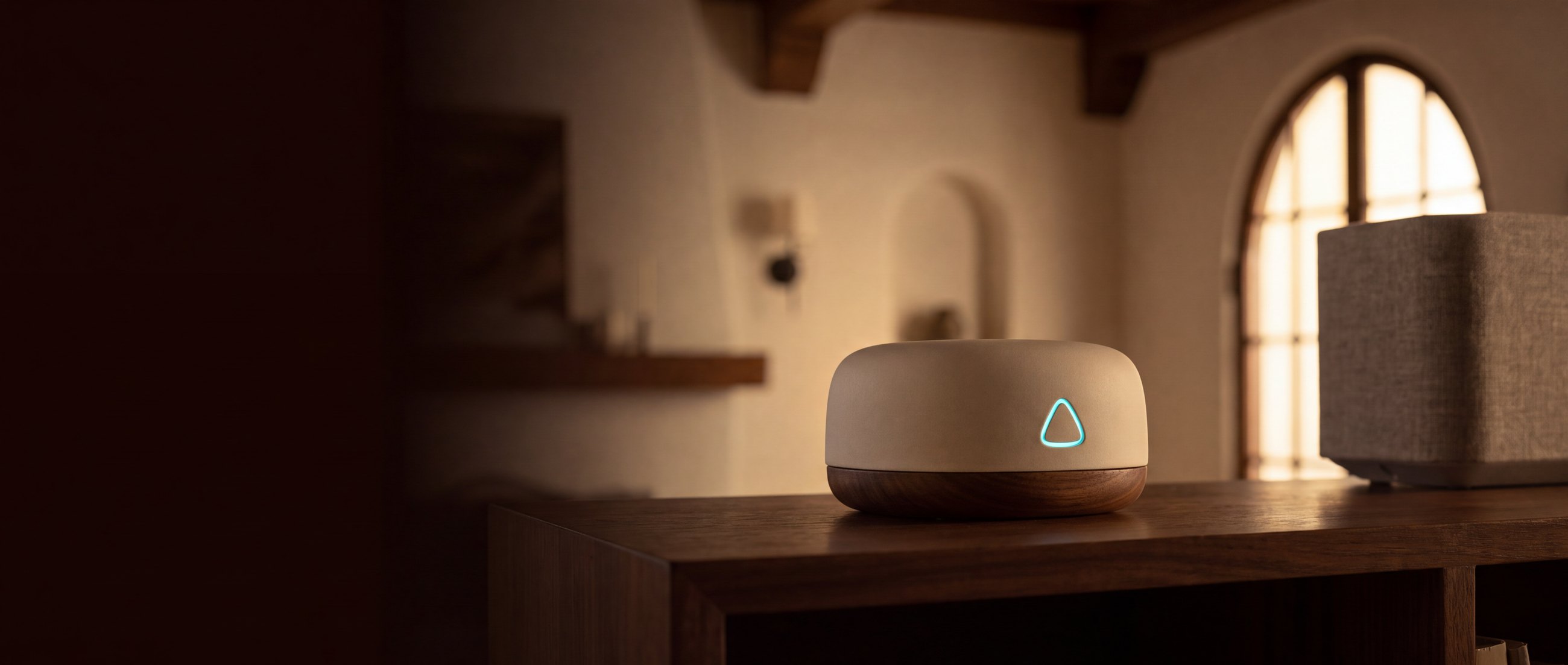 The ALYT Voice satellite on a walnut shelf at dusk, its triangular light glowing.