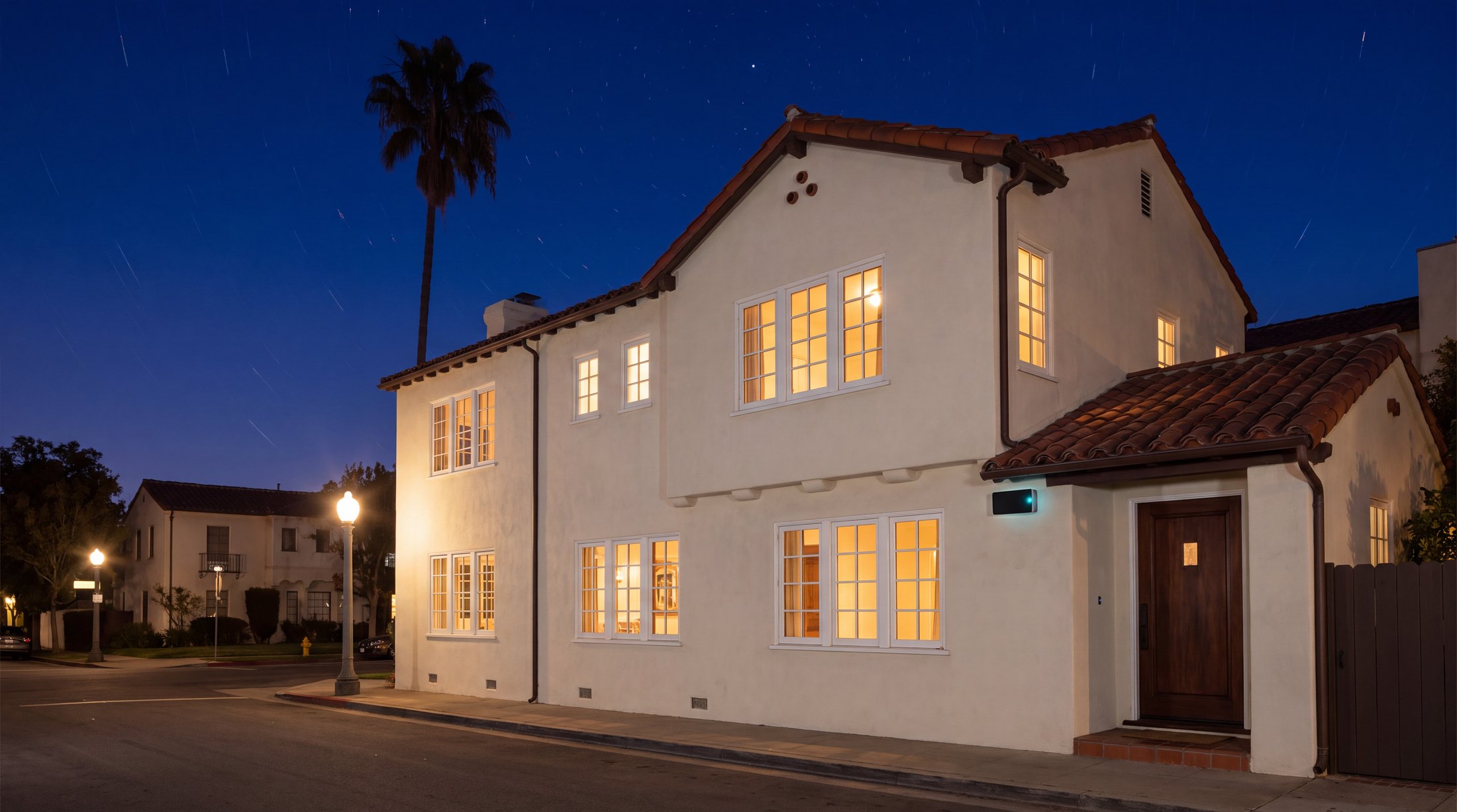 A Spanish-revival house at night, windows glowing warm, quietly protected.